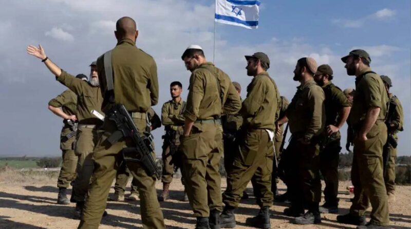 Soldiers stand near an Israeli flag as they receive a briefing near the border