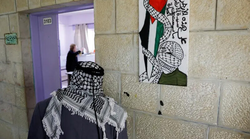 A man wearing a Palestinian keffiyeh stands next to a poster